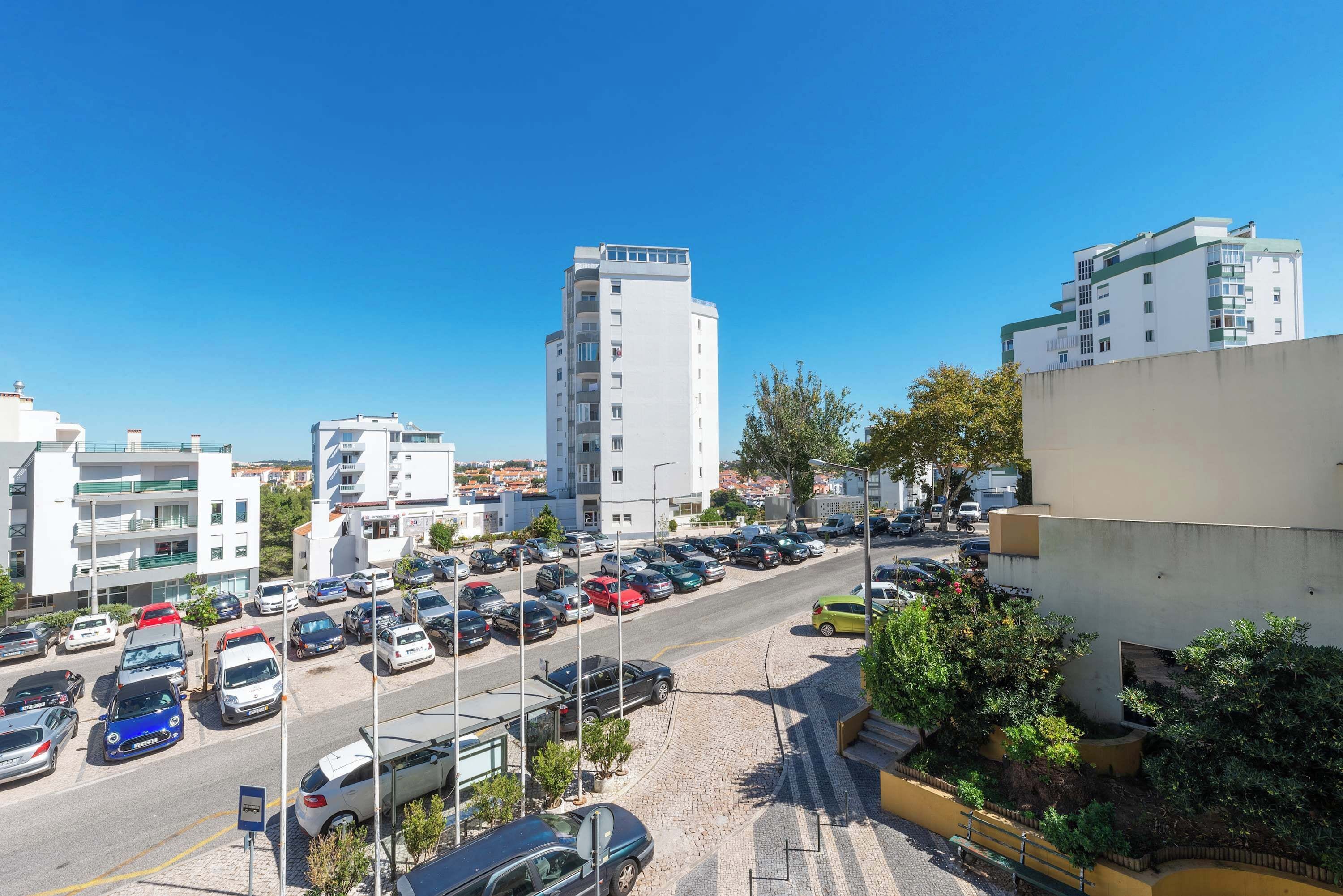 Un parking rempli de voitures, un ciel bleu dégagé et des bâtiments en arrière-plan.