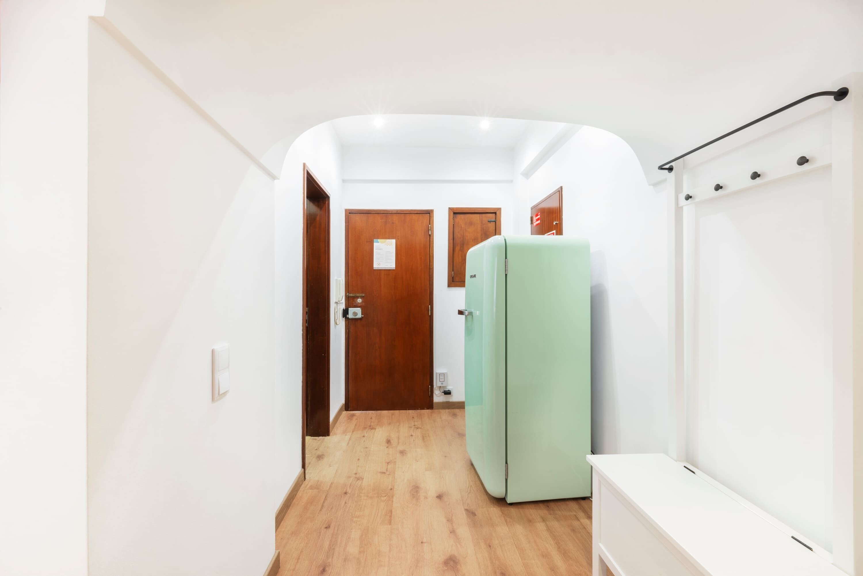 A narrow hallway with wooden flooring, white walls, and a green refrigerator.