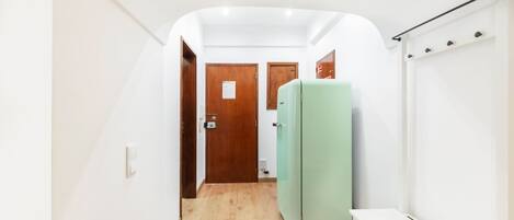 A narrow hallway with wooden flooring, white walls, and a green refrigerator.