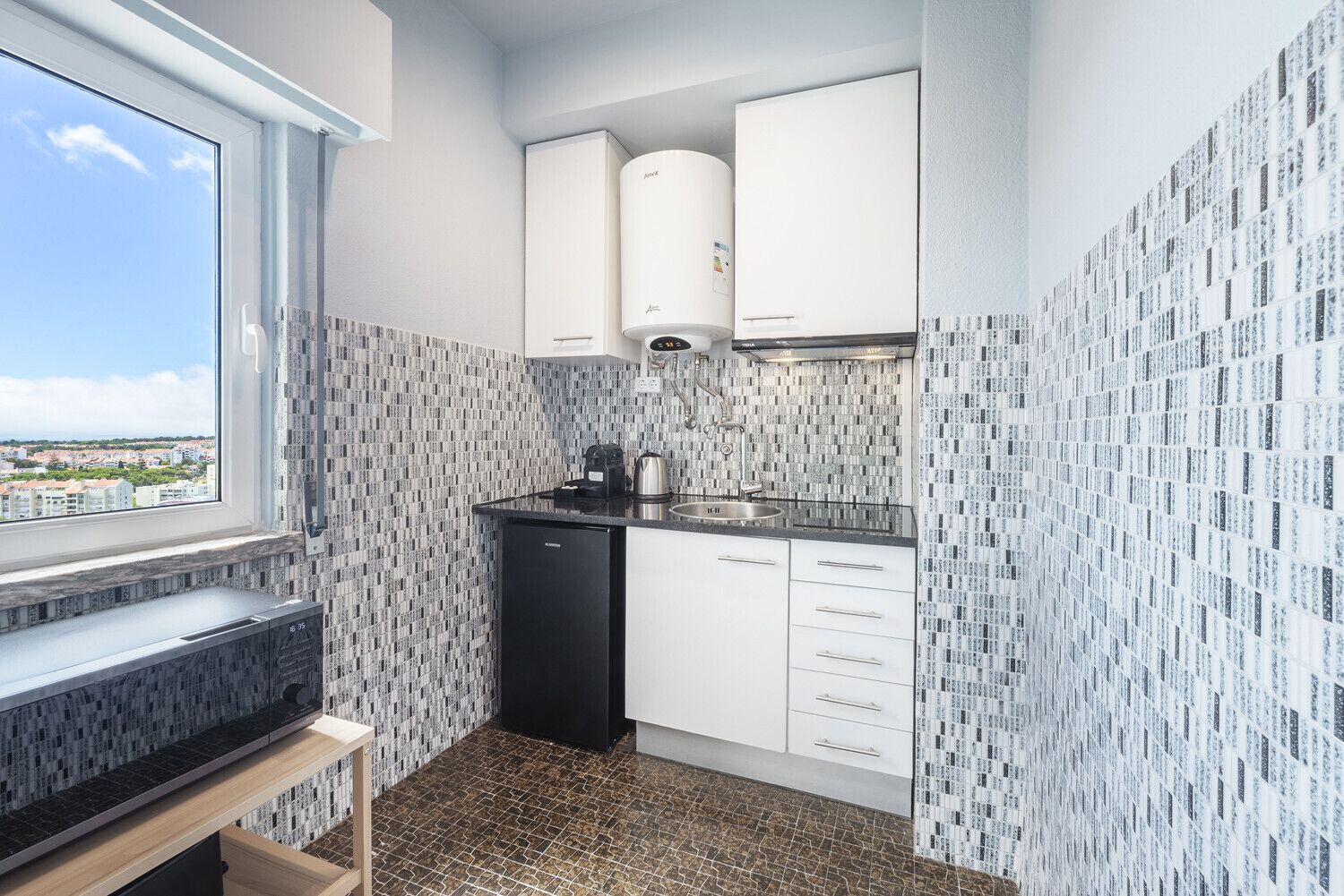A compact kitchen with white cabinets, a black dishwasher, and a window overlooking a cityscape.