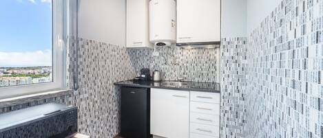 A compact kitchen with white cabinets, a black dishwasher, and a window overlooking a cityscape.