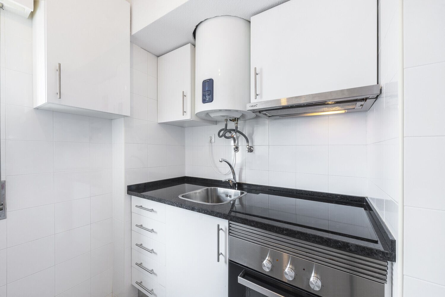 A compact kitchen with white cabinets, a stainless steel sink, and a built-in oven.