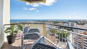 A balcony with two wicker chairs, a potted plant, and a view of the city and sea. - Equador Studios by Olala Homes (Cascais)