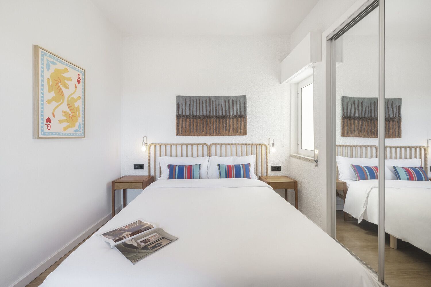 Ein Hotelzimmer mit einem großen Bett, zwei Nachttischen, einem Spiegel und einem gerahmten Bild an der Wand.