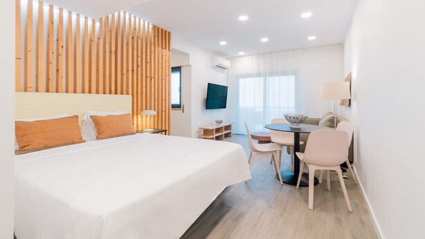 A modern hotel room with a large bed, a desk with a chair, a TV, and a window with curtains. - Equador Studios by Olala Homes (Cascais)