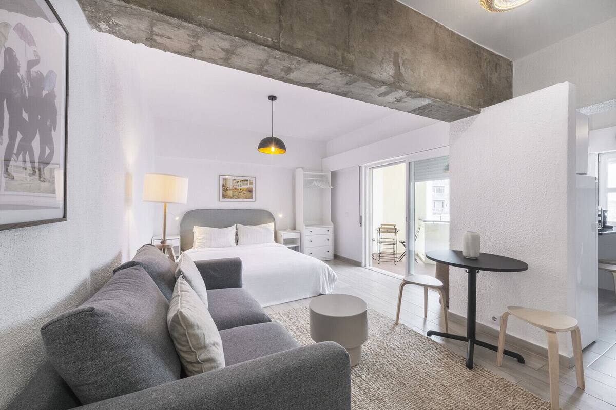 Een moderne hotelkamer met een bed, een bank, een klein tafeltje en een stoel. Er is een balkon met uitzicht over de stad.