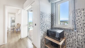 A modern apartment with a kitchen area, a dining area with a chair, and a view of the city through a window. - Equador Studios by Olala Homes (Cascais)