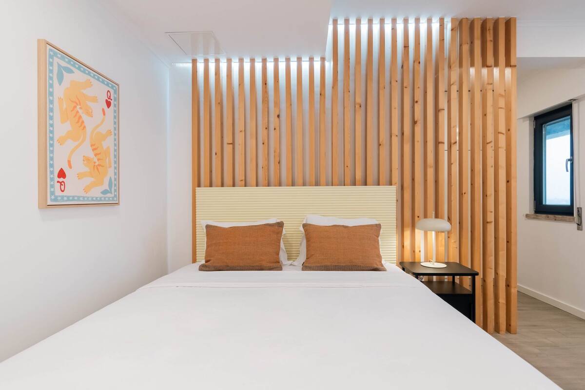 Een moderne slaapkamer met een groot bed, twee kussens, een nachtkastje, een lamp en een wand van houten latten.