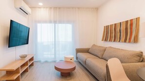 A modern living room with a sofa, a round coffee table, a TV mounted on the wall, and a striped artwork. - Equador Studios by Olala Homes (Cascais)