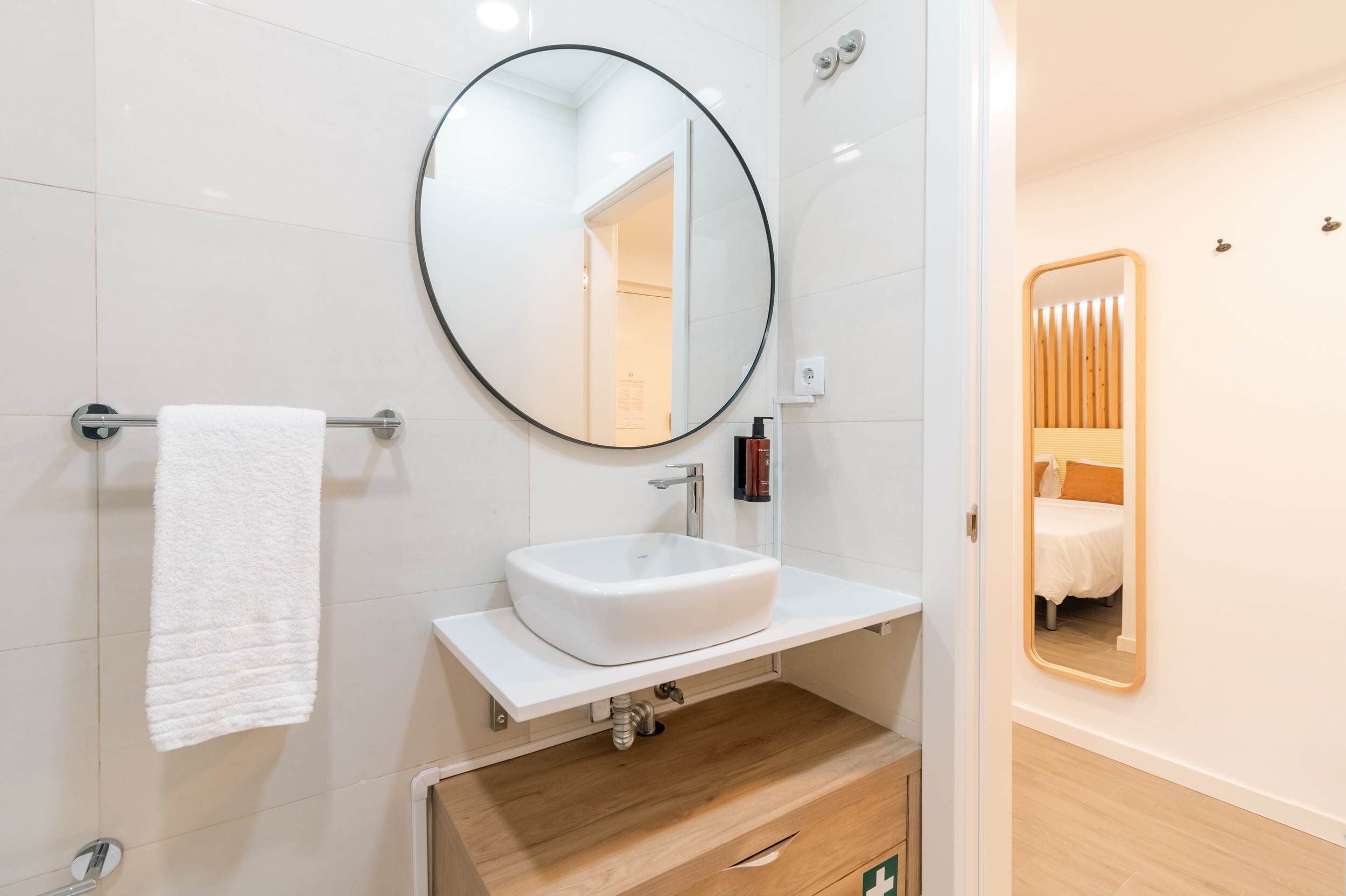Une salle de bain moderne avec un lavabo blanc, un miroir rond et un porte-serviettes.