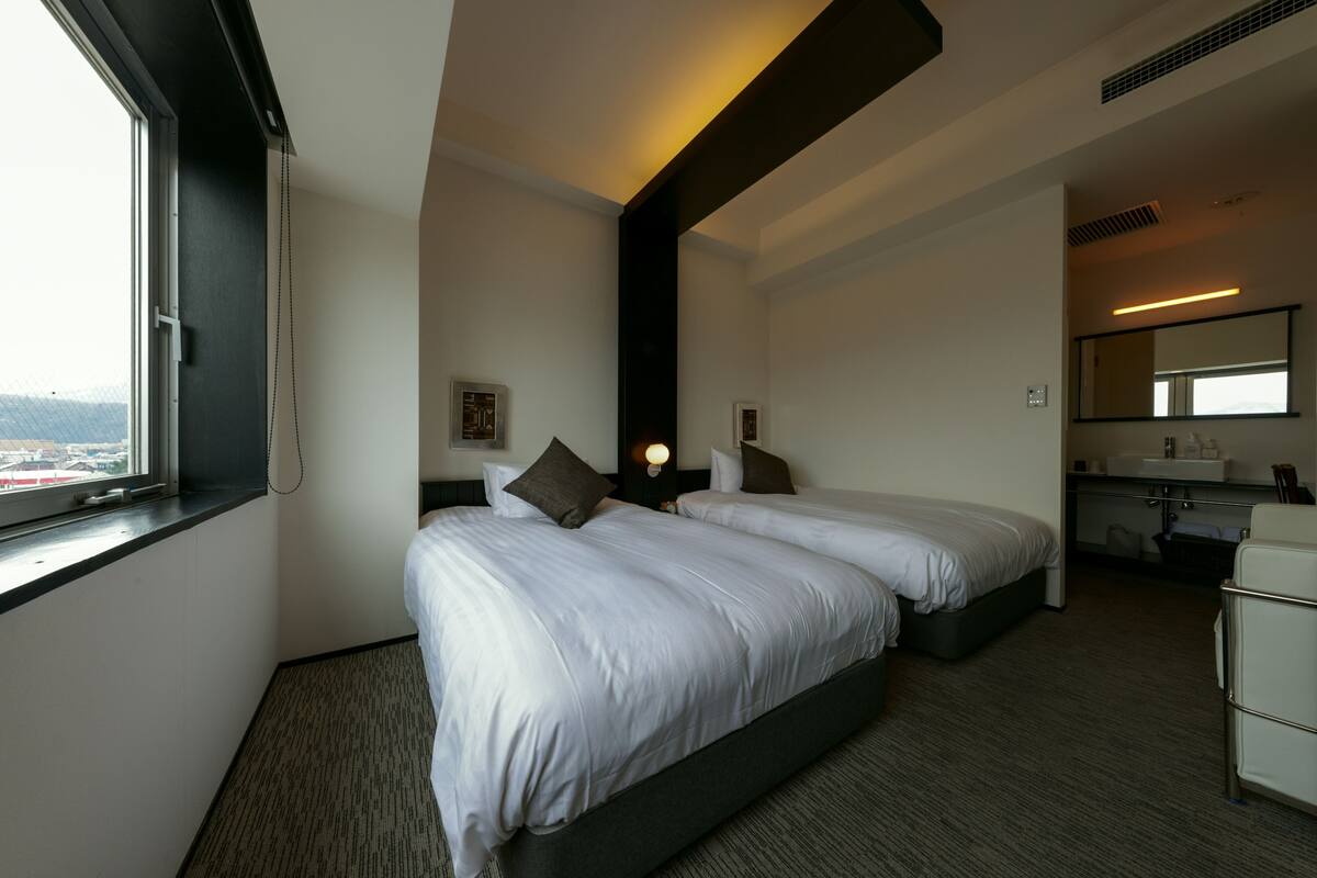 Habitación de hotel con dos camas, una ventana, un escritorio y un baño.