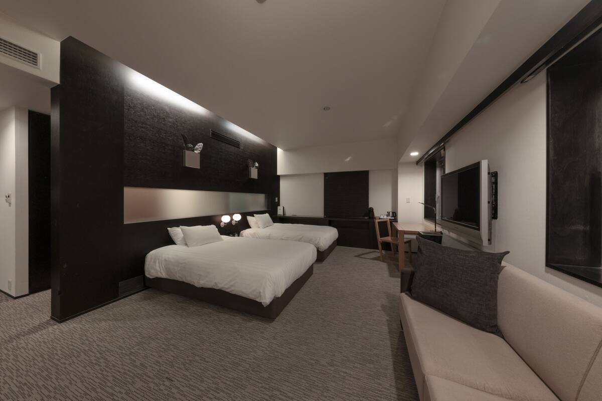 Habitación de hotel moderna con dos camas, un sofá, un televisor y un escritorio.