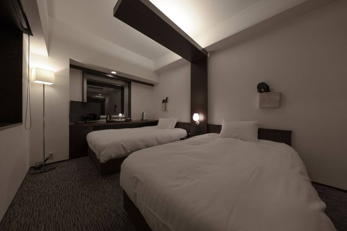 Una habitación de hotel con dos camas, un escritorio, un espejo y una lámpara.