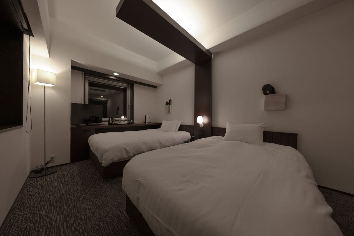 Ein Hotelzimmer mit zwei Betten, einem Schreibtisch, einem Spiegel und einer Lampe.