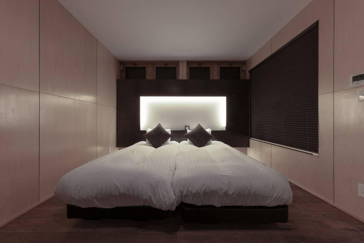 Un dormitorio moderno con una cama grande, un televisor montado en la pared y una ventana con persianas.