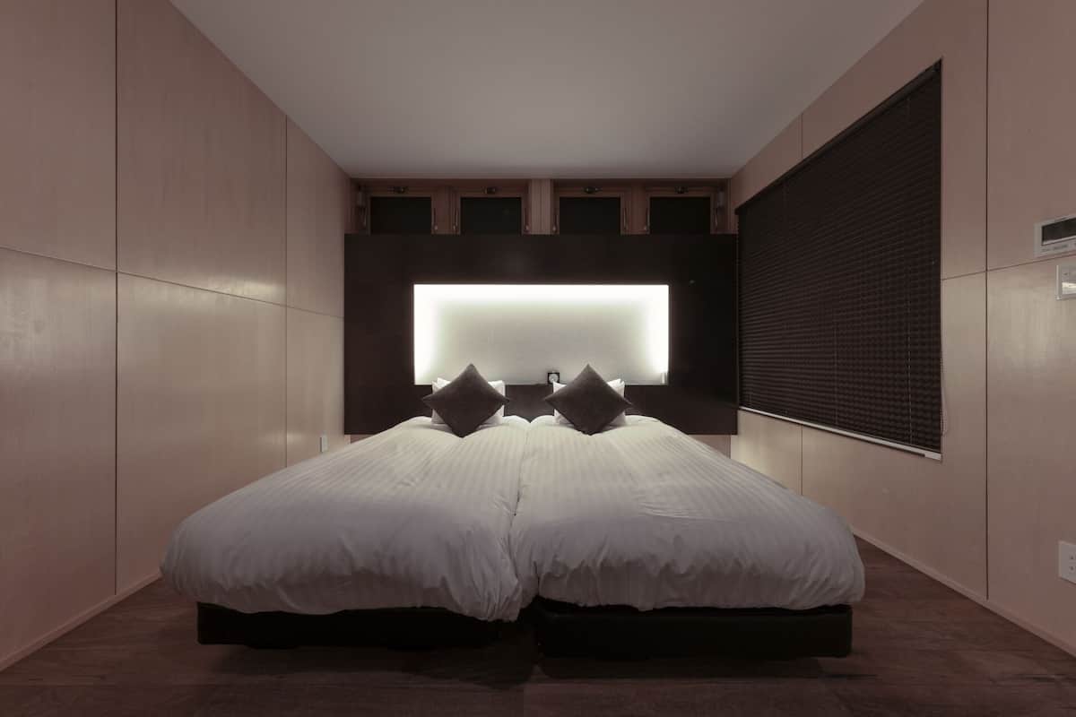 Ein modernes Schlafzimmer mit einem großen Bett, einem an der Wand befestigten Fernseher und einem Fenster mit Jalousien.