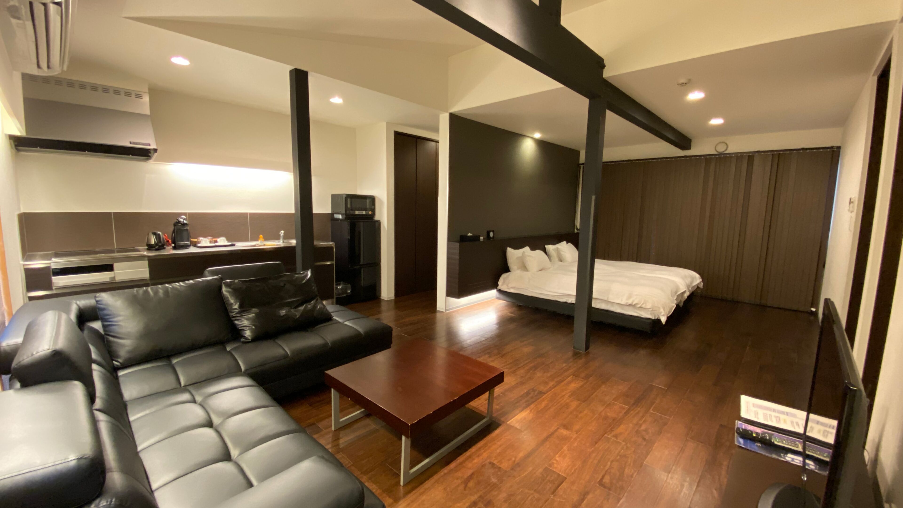 A modern living room with a sofa, a coffee table, a bed, and a kitchen area with a stove and cabinets.