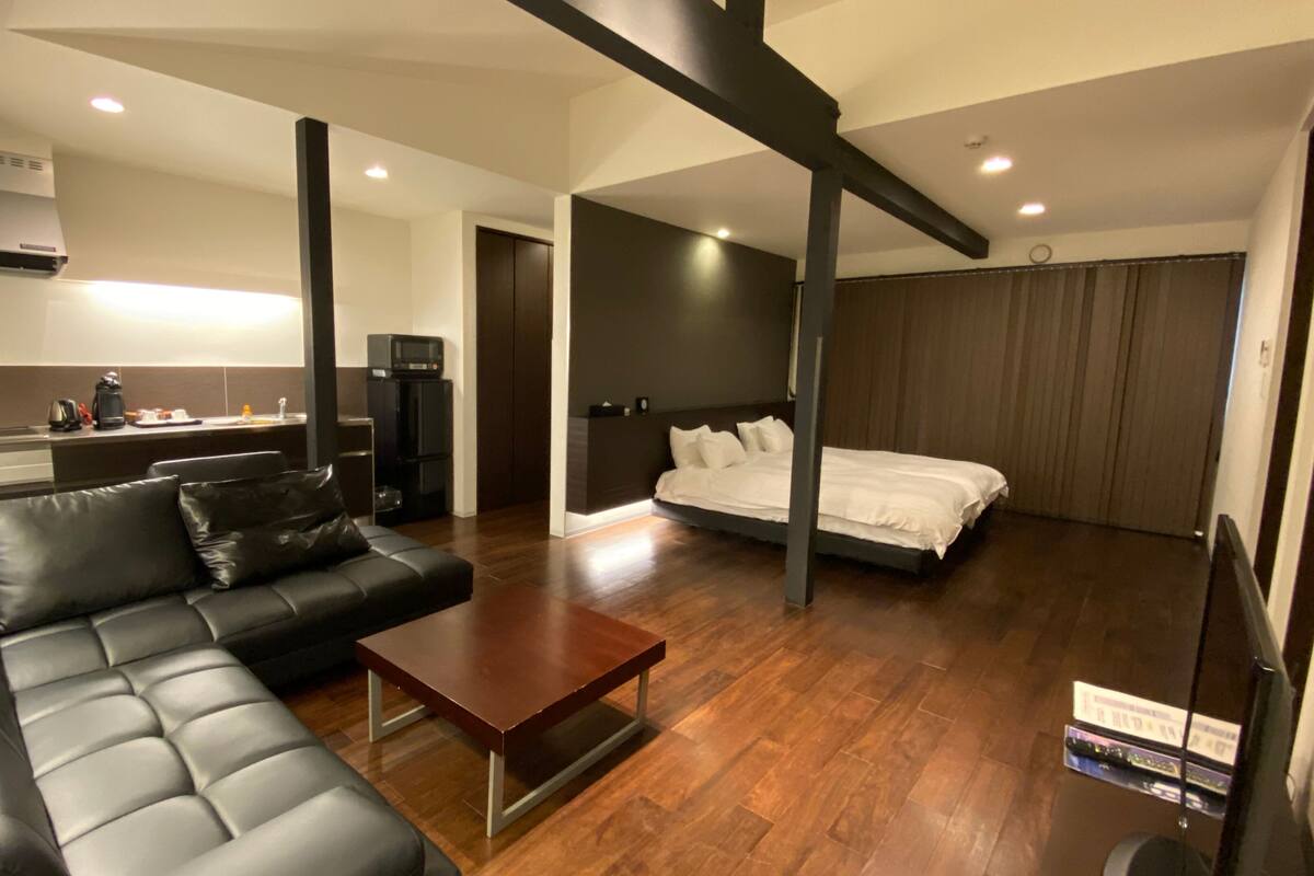 Una sala moderna con sofá, mesa de centro, cama y área de cocina con estufa y armarios.