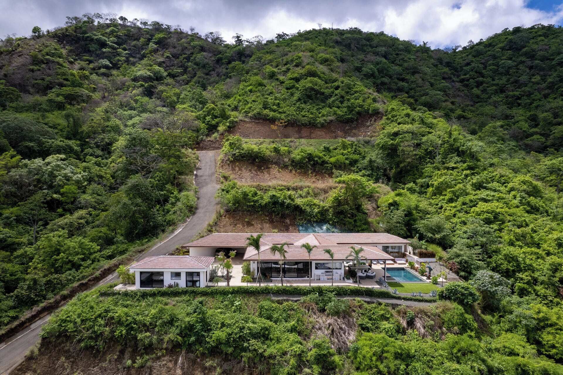 A modern house with a swimming pool, surrounded by lush greenery and hills.