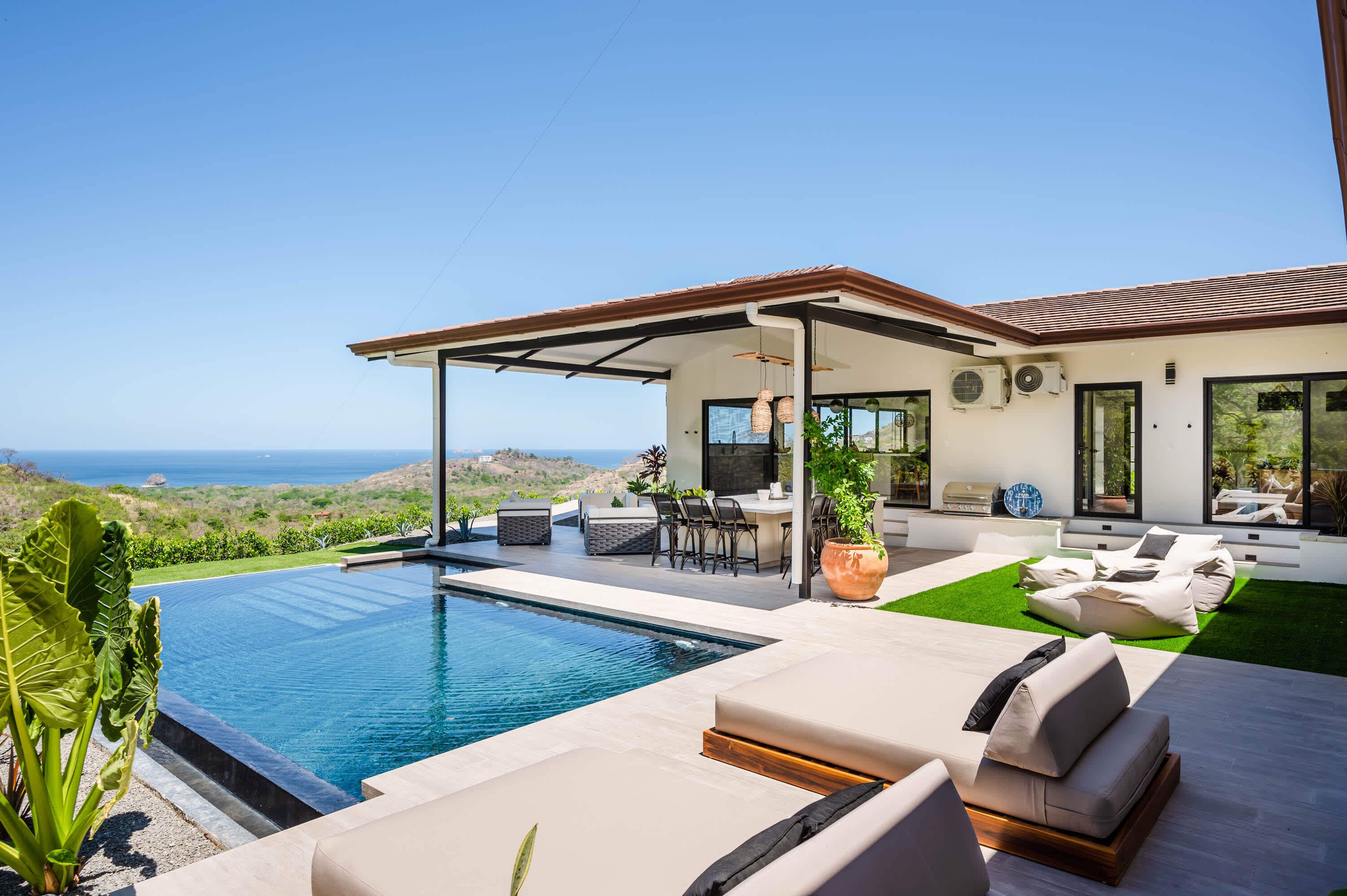 Ein modernes Haus mit Swimmingpool, Sitzgelegenheiten im Freien und Meerblick.