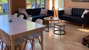 Un salon spacieux doté d’un plancher en bois, de deux canapés, d’une table à manger et de grandes fenêtres offrant une vue sur les arbres.