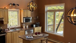 Une cuisine spacieuse, dotée de meubles en bois, d’un îlot central et de grandes fenêtres offrant une vue sur l’extérieur.