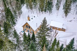 Une cabane à deux étages, dont le toit est recouvert de neige, entourée d’une forêt.