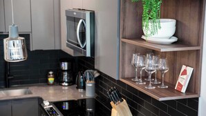 Una cocina moderna con microondas, lámpara colgante, bloque de cuchillos y estante con copas de vino y una planta.