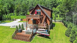 Une cabane à deux étages dotée d’un balcon, entourée d’une pelouse bien entretenue et d’arbres.