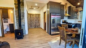 A modern kitchen with a large refrigerator, wooden dining table, and a stone fireplace. - Hot Tub, Lake Front, NEW Game Rm, Fire Pit, Kayaks (Eureka Springs)