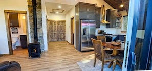 A modern kitchen with a large refrigerator, wooden dining table, and a stone fireplace.