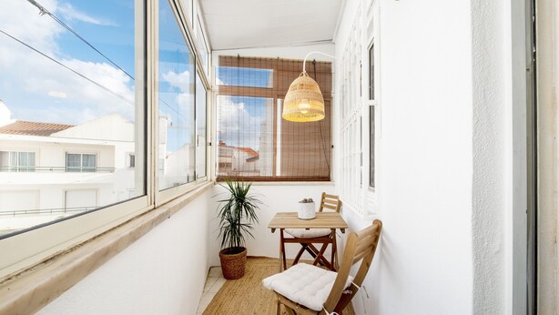 A small balcony with a table and chairs, a hanging light fixture, a potted plant, and a view of buildings outside. - Navegantes Townhouse by Olala Homes. (Cascais)