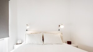 A minimalist bedroom with a large bed, two bedside lamps, and a small bedside table with a red object. - Navegantes Townhouse by Olala Homes. (Cascais)