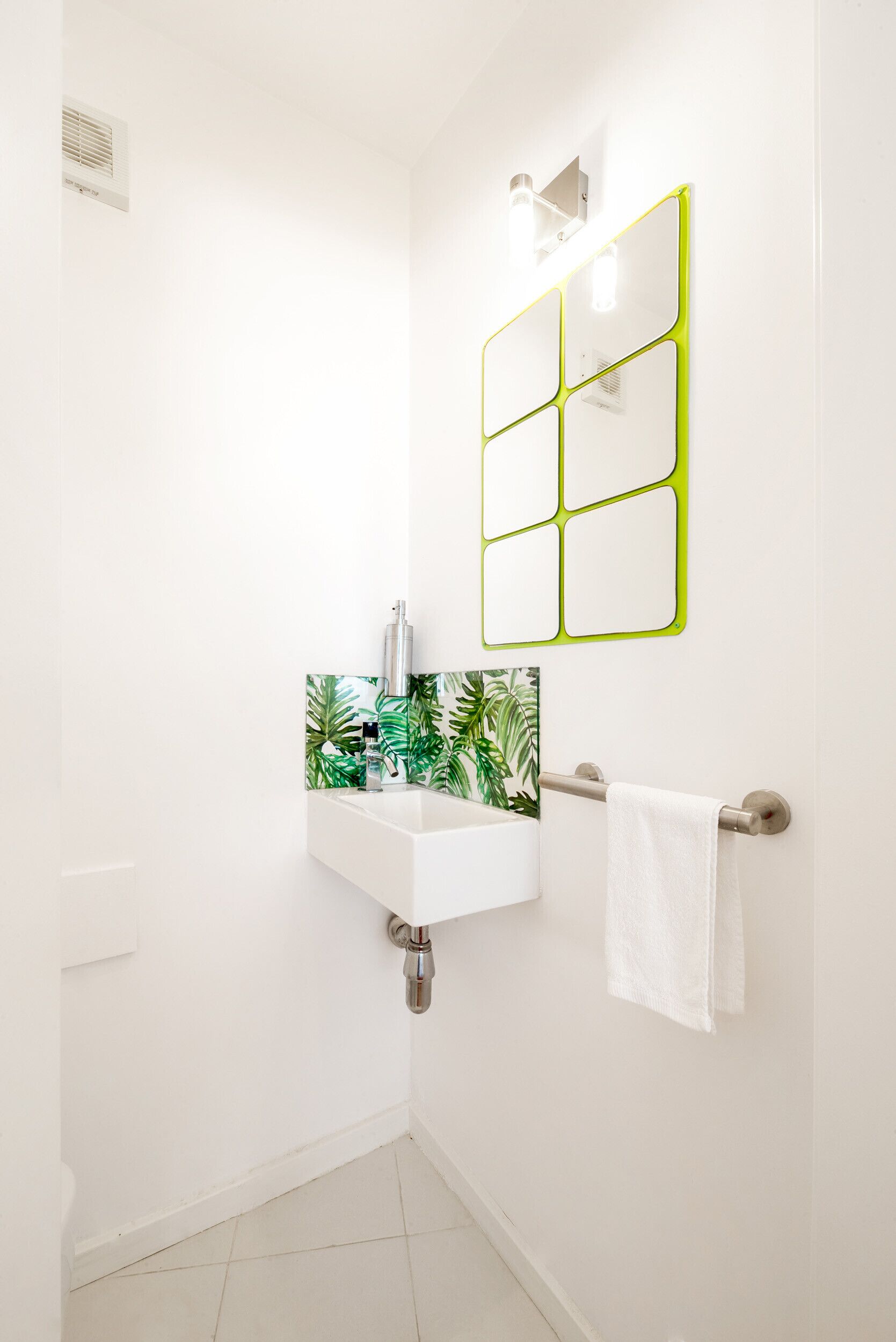 A bathroom with a white sink, a mirror with a green frame, and a towel hanging on a towel rack.