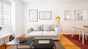 A modern living room with a sofa, two framed artworks, a floor lamp, a dining table, and a coffee table. - Navegantes Townhouse by Olala Homes. (Cascais)