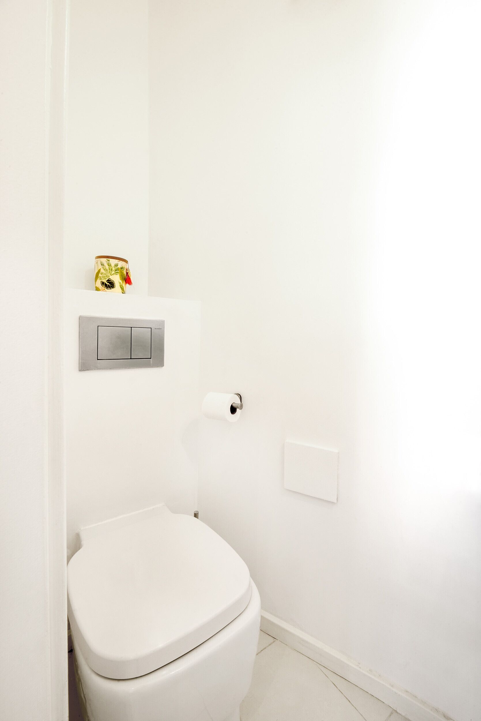 A white bathroom with a toilet, a toilet paper holder, and a light switch.