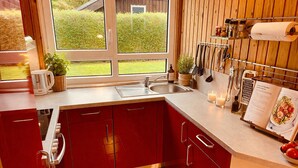 Una cocina con armarios rojos, un lavamanos de acero inoxidable y una ventana con vistas a un jardín.