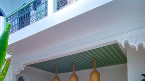 Un espace extérieur spacieux avec un canapé blanc, des fauteuils en osier et une table. On y trouve des lampes suspendues, des plantes en pot et un sol carrelé.