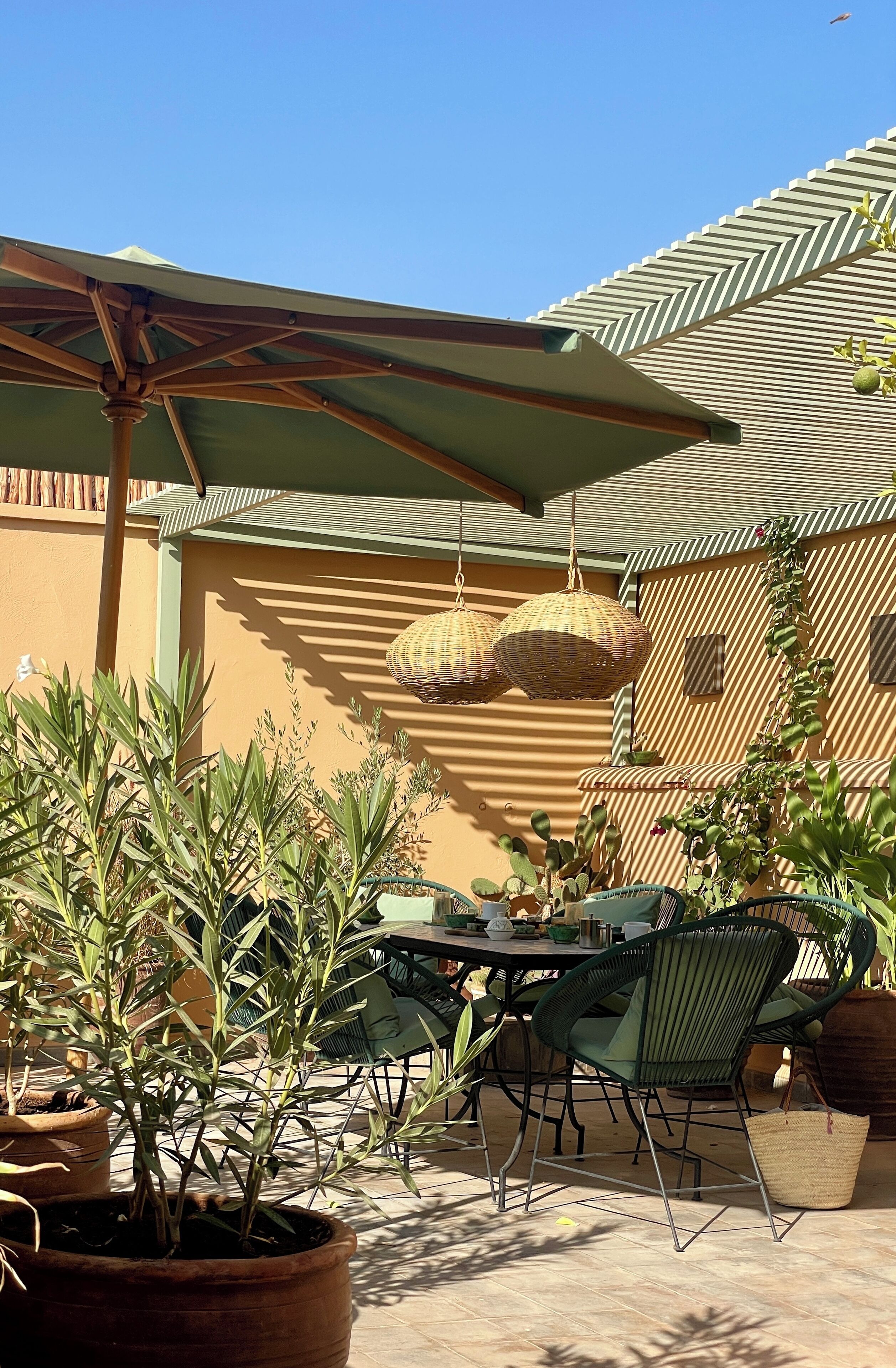 Eine Terrasse im Freien mit Tisch und Stühlen, umgeben von Topfpflanzen und einem hängenden Korb.