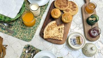 A breakfast setting with a variety of food items, including pancakes, apple slices, and beverages, arranged on a table with a hexagonal tile floor.