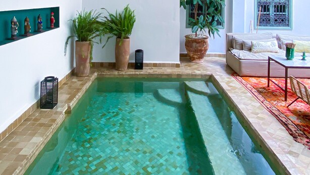Un espace piscine doté d’un sol carrelé, d’un canapé et de paniers en osier suspendus.