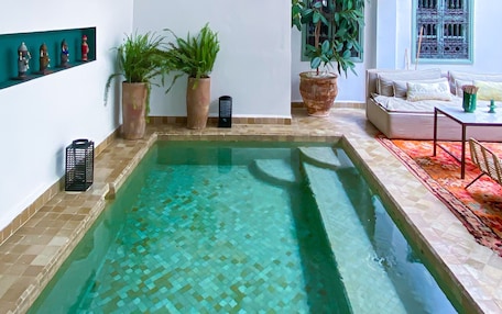 A pool area with a tiled floor, a sofa, and hanging wicker baskets.