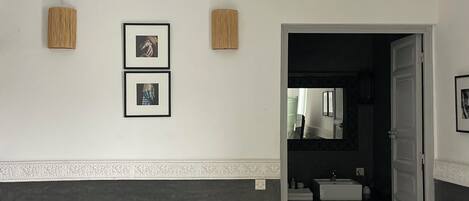 Una sala de estar con un sofá, una mesa de centro de vidrio, una lámpara de techo de mimbre y cuadros en la pared.