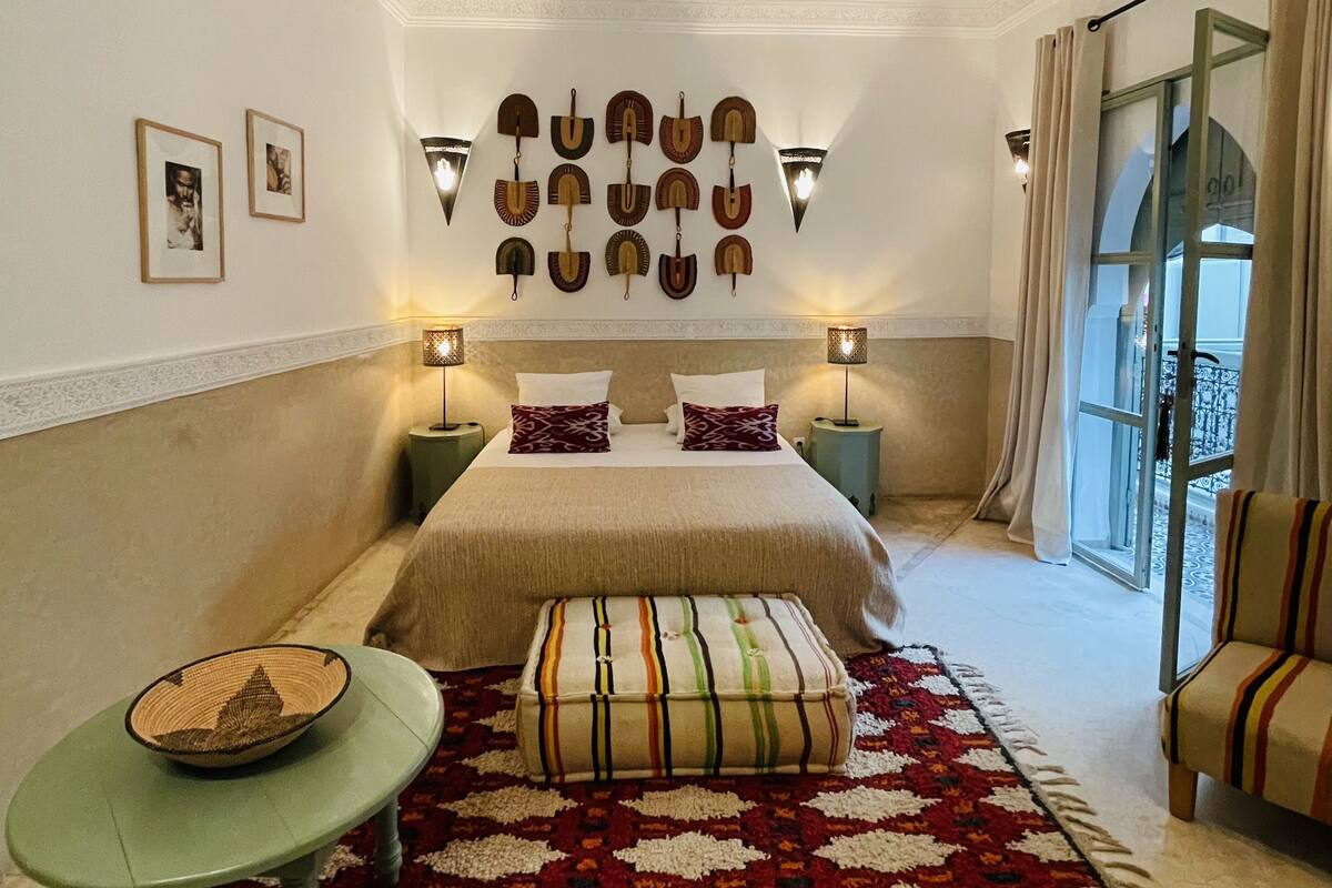 A bedroom with a large bed, two bedside tables with lamps, a small table with a bowl, a colorful rug, and a chair.