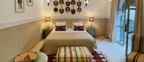 A bedroom with a large bed, two bedside tables with lamps, a small table with a bowl, a colorful rug, and a chair.