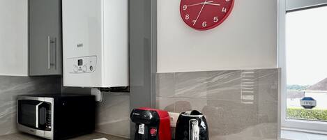 A kitchen with a Bosch coffee maker, a microwave, and a red clock on the wall.