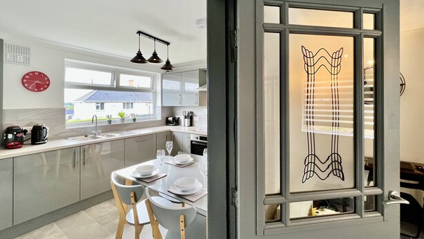A modern kitchen with a dining area, a large window, and a decorative door with a unique design. - Havenwood House (Nottingham)