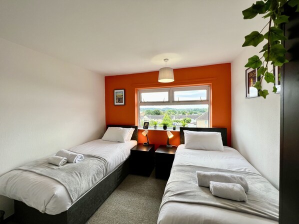 A hotel room with two single beds, a window with a view of the city, a small table with a lamp, and a picture on the wall.
