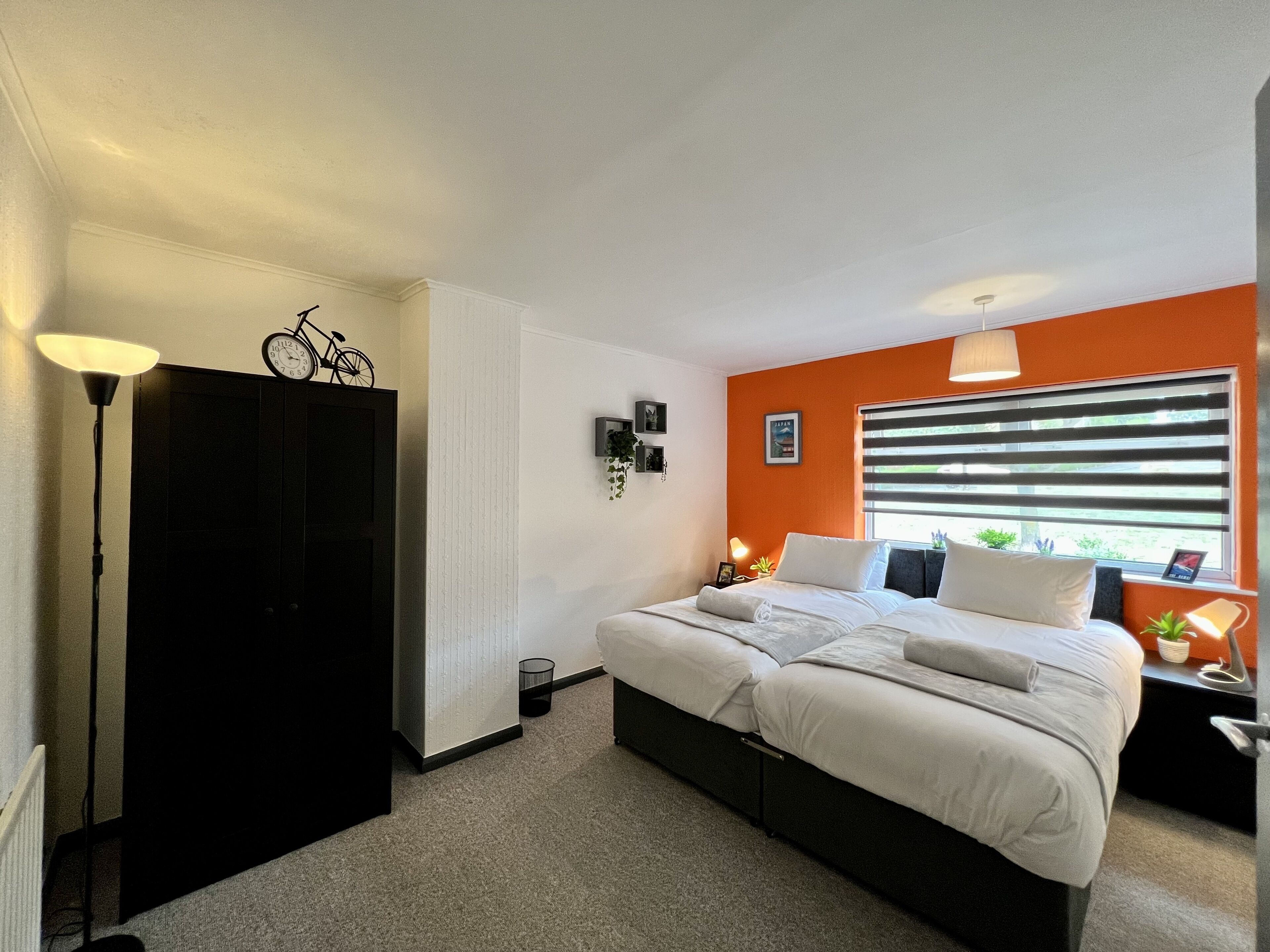 A bedroom with a bed, a nightstand, a lamp, a bicycle on the wall, and a window with blinds.