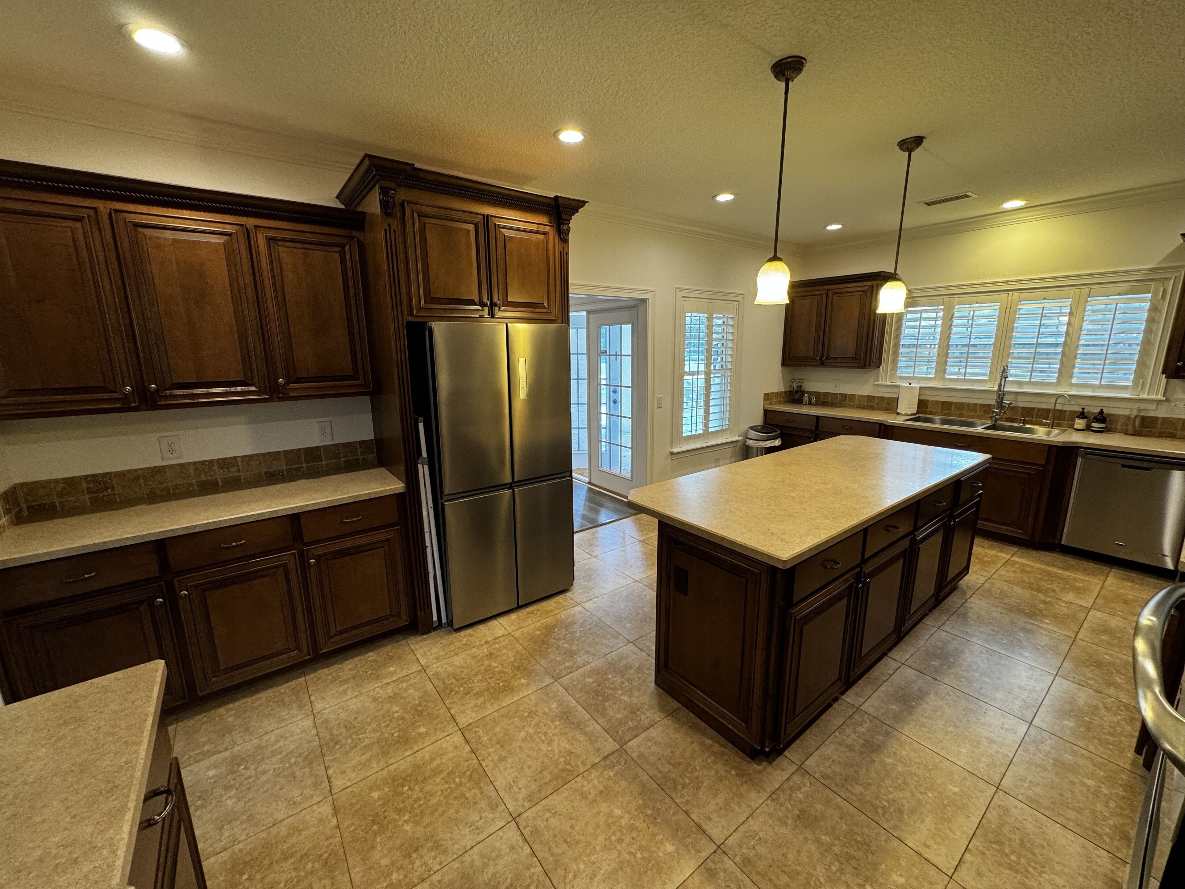 Una cocina moderna con armarios de madera, un refrigerador de acero inoxidable, una isla grande e iluminación colgante.